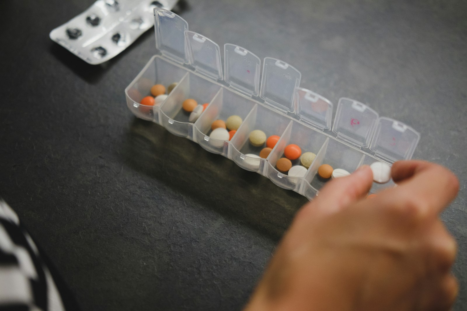 Hand taking supplements from a weekly pill organizer